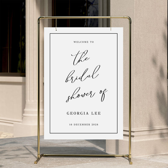 Welcome sign for a bridal shower with a gold stand against a neutral wall.