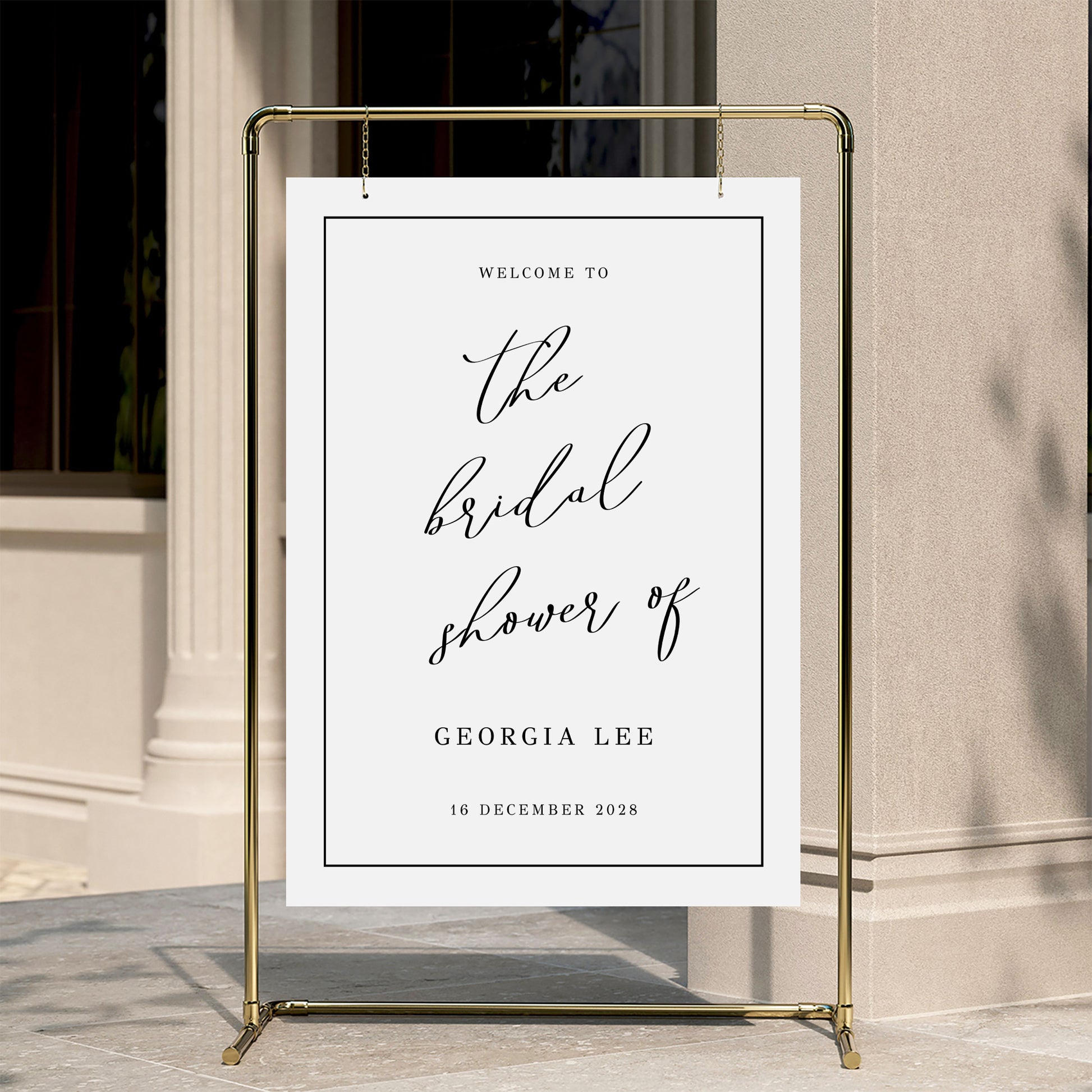 Welcome sign for a bridal shower with a gold stand against a neutral wall.