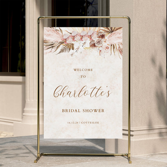 Floral bridal shower welcome sign on a stand against a neutral wall.