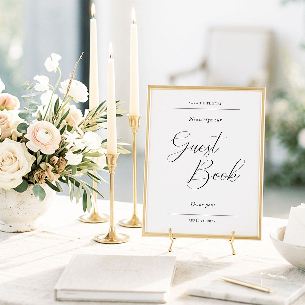 Printable guest book wedding sign in a gold frame on a small easel, beside taper candles, blush roses and a fabric guest book.