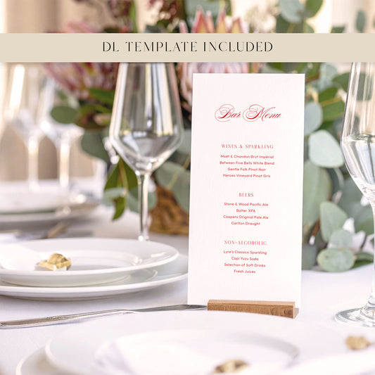 Wedding bar menu card with drink options on a wooden holder sitting on a white table cloth with flowers, plates and wine glasses.
