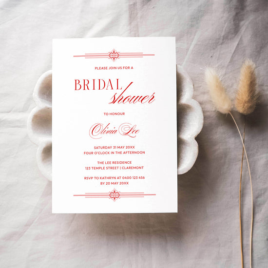 Red bridal shower invitation template on a textured surface with dried flowers.