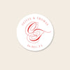 Round white invitation seal with red monogram text on a beige background.