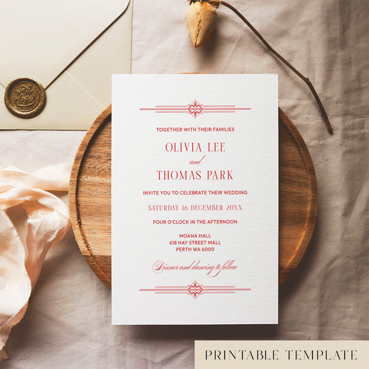Red old money style wedding invitation template design on a white card sitting on a wooden plate with decorative elements.