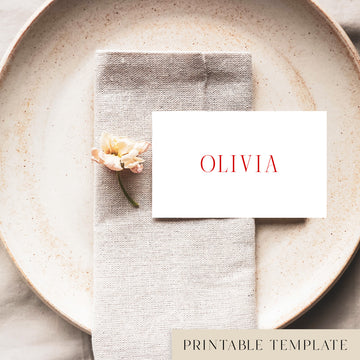 A flat place card with a name printed on it, positioned on a plate with a napkin and a floral decoration.