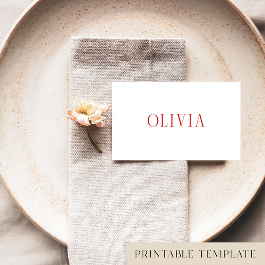 A flat place card with a name printed on it, positioned on a plate with a napkin and a floral decoration.