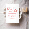 Old-money style save the date card with red text on a white background, placed on a textured surface with dried plants.