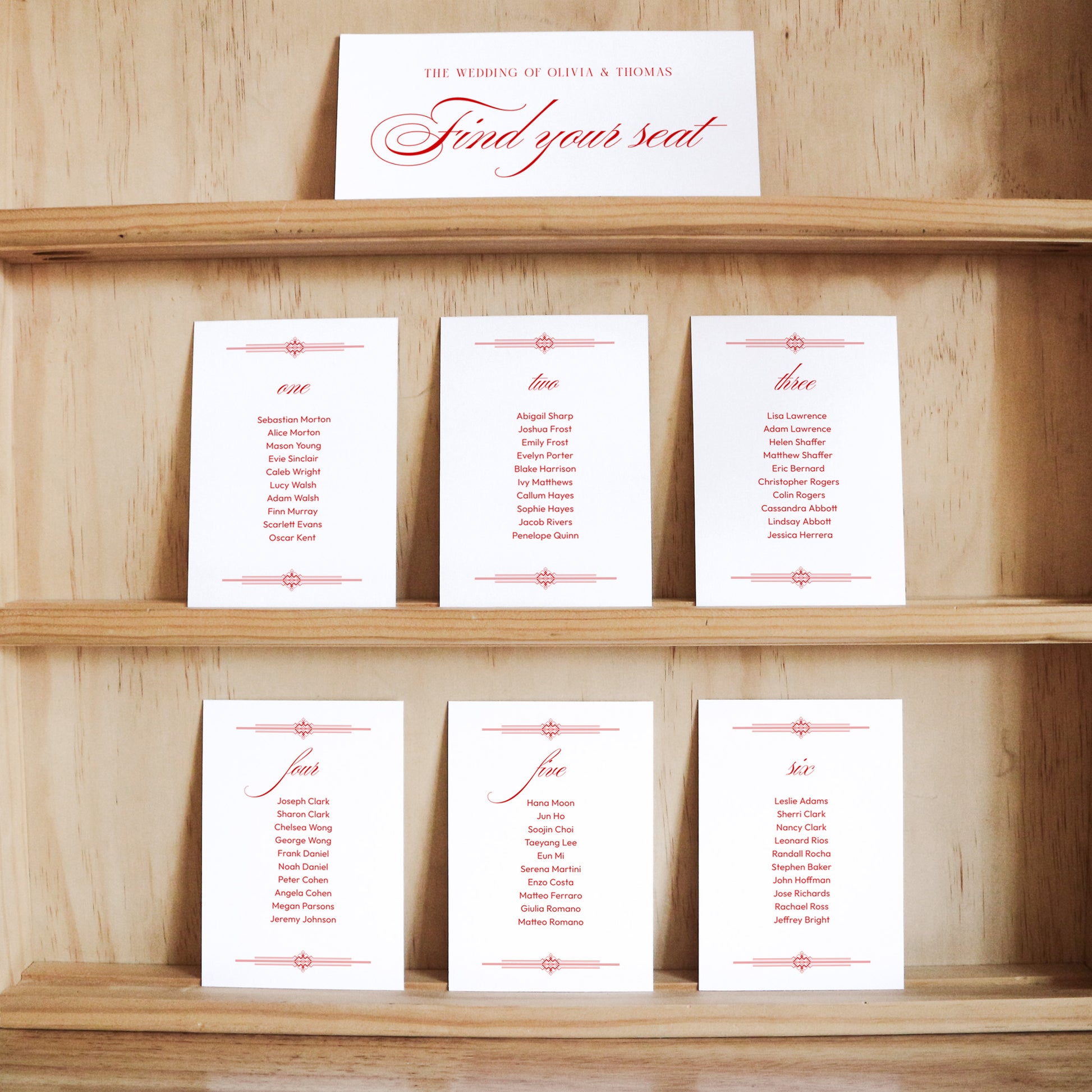 Set of white seating cards with names and table numbers on a wooden shelf with a title card at the top.