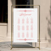 Wedding seating chart template displayed on a gold stand against a neutral wall.