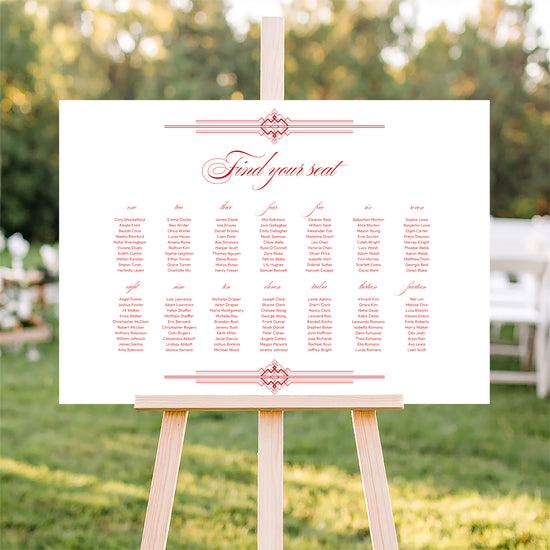 Horizontal wedding seating plan sign on an easel with a blurred outdoor ceremony background.