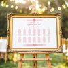 Decorative gold frame on an easel with a horizontal wedding seating chart outdoors.