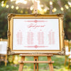 Decorative gold frame on an easel with a horizontal wedding seating chart outdoors.