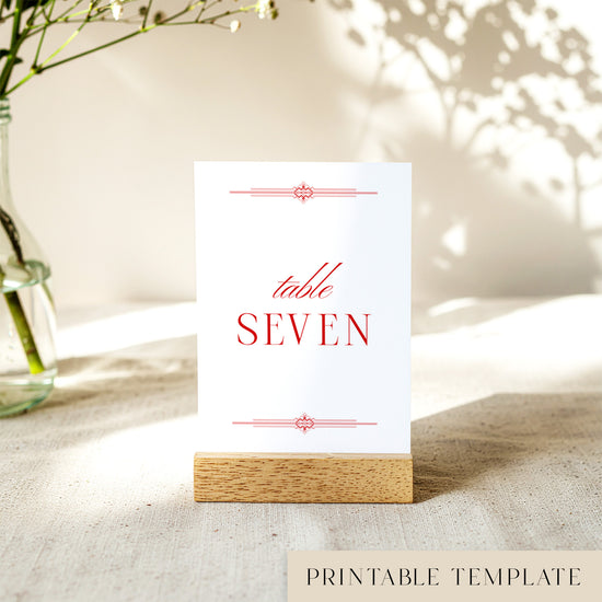 Printable table number card displayed on a wooden stand with a blurred natural background.