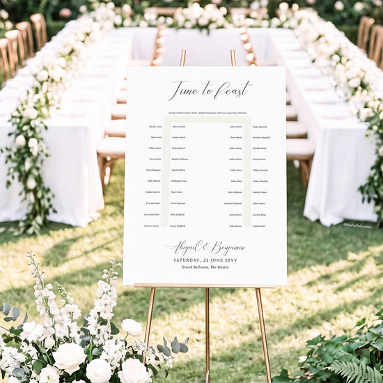 Elegant horseshoe wedding seating chart template shown on a gold easel in front of a floral-lined reception table.