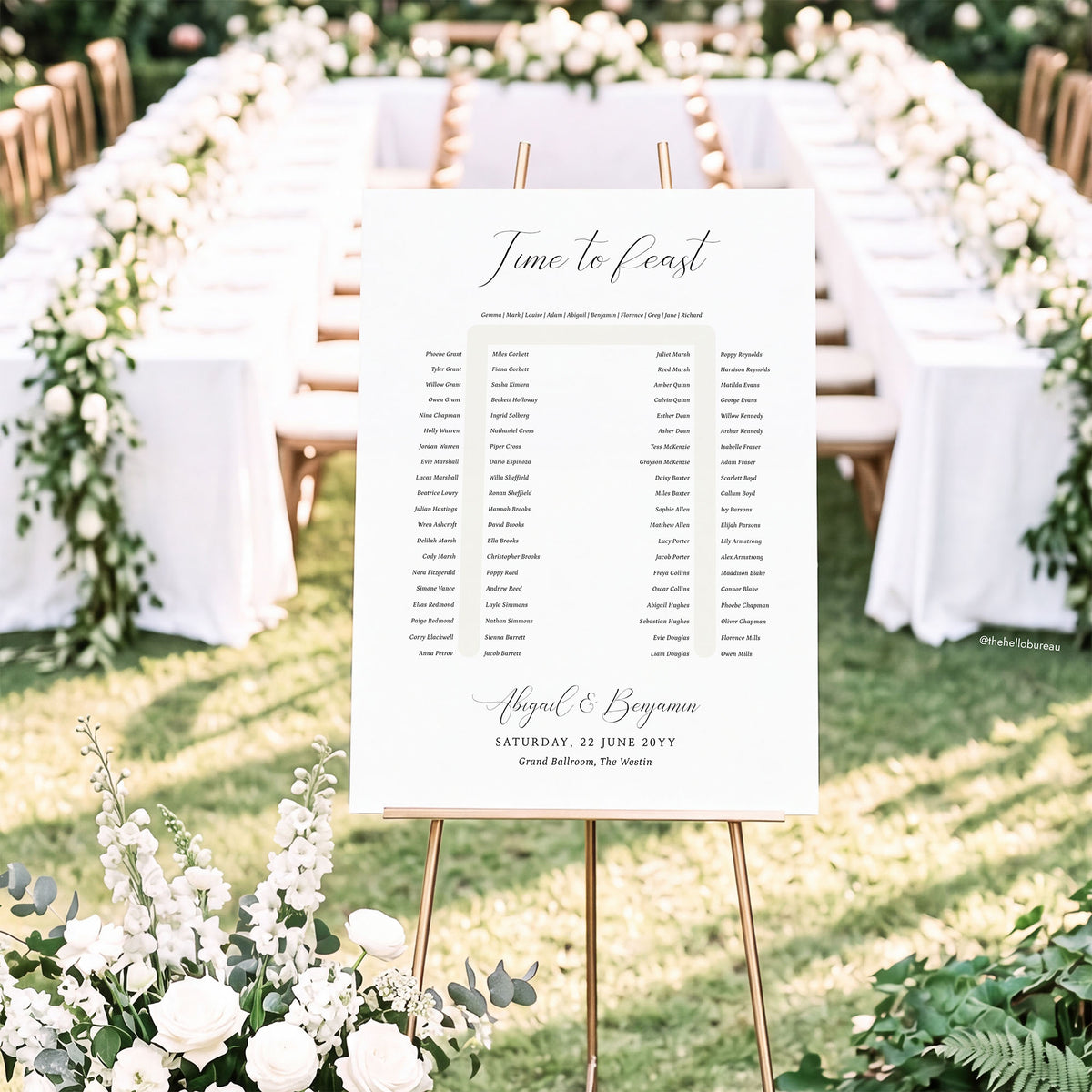 Elegant horseshoe wedding seating chart template shown on a gold easel in front of a floral-lined u-shape table.