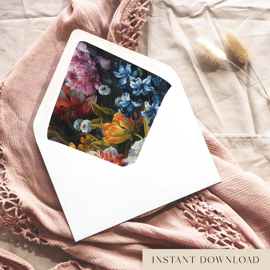 Printable moody floral envelope liner for 5x7 wedding invitations, with a painted still life of blue hyacinths, pink peony blooms and orange tulips on a deep charcoal background, shown inside a white envelope on dusty pink fabric.