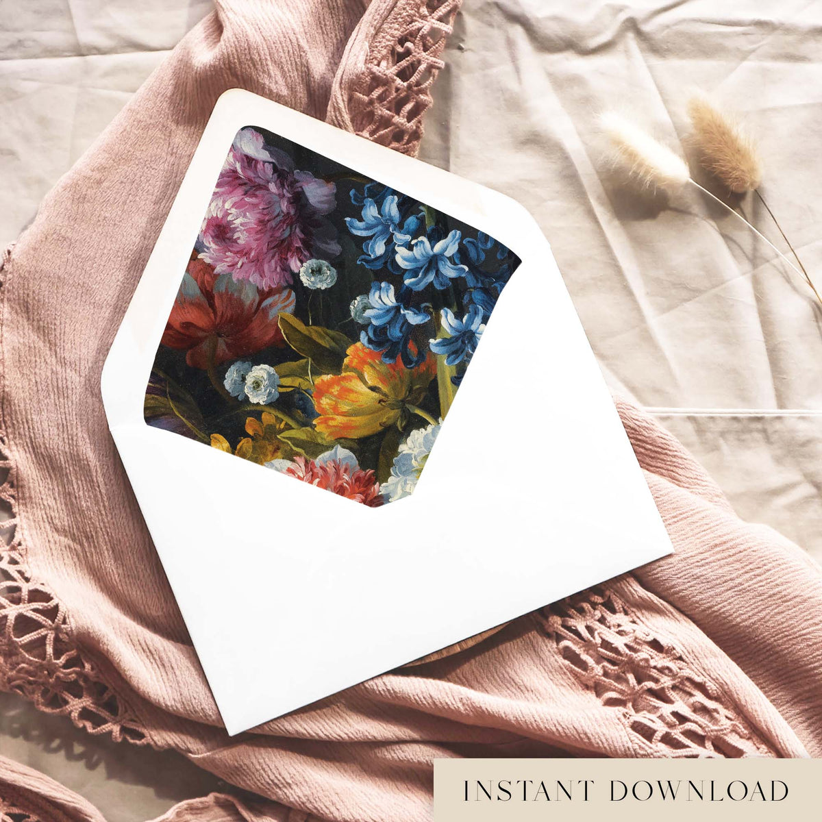 Printable moody floral envelope liner for 5x7 wedding invitations, with a painted still life of blue hyacinths, pink peony blooms and orange tulips on a deep charcoal background, shown inside a white envelope on dusty pink fabric.