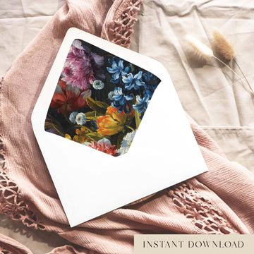 Printable moody floral envelope liner for 5x7 wedding invitations, with a painted still life of blue hyacinths, pink peony blooms and orange tulips on a deep charcoal background, shown inside a white envelope on dusty pink fabric.