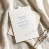 Wedding invitation card on textured card with envelope on fabric background.
