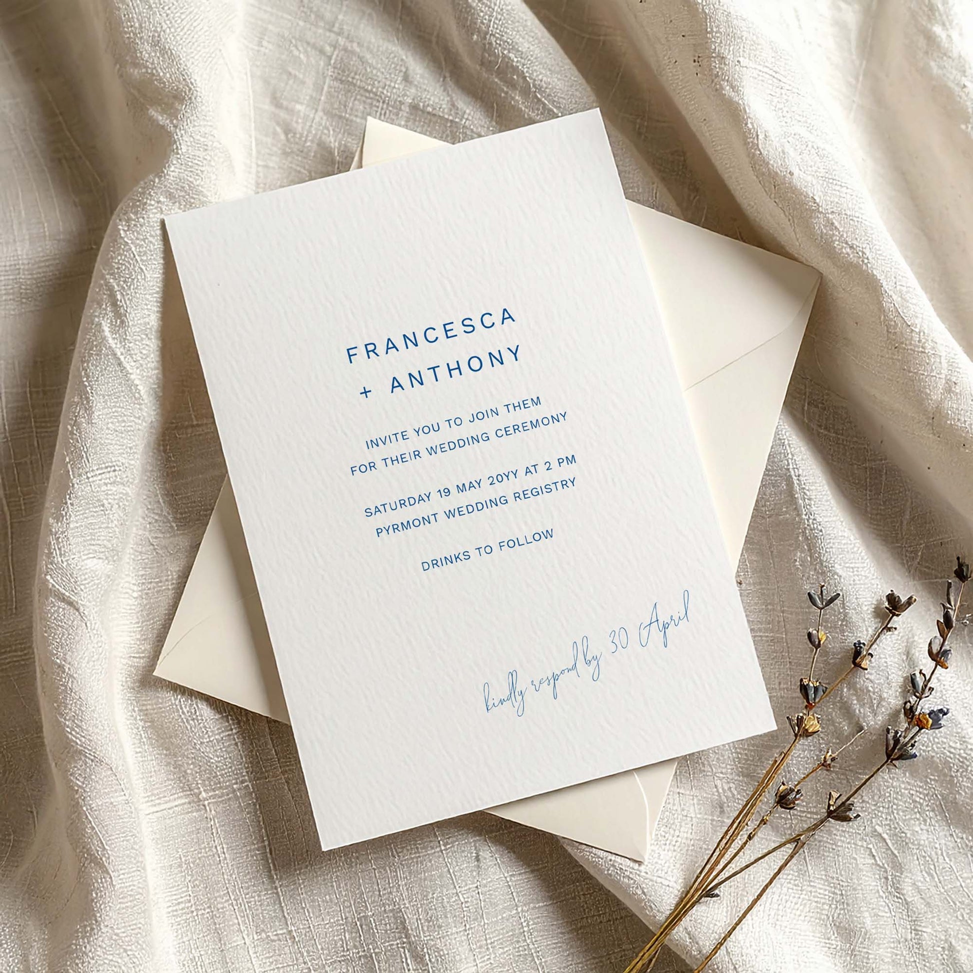 Wedding invitation card on textured card with envelope on fabric background.
