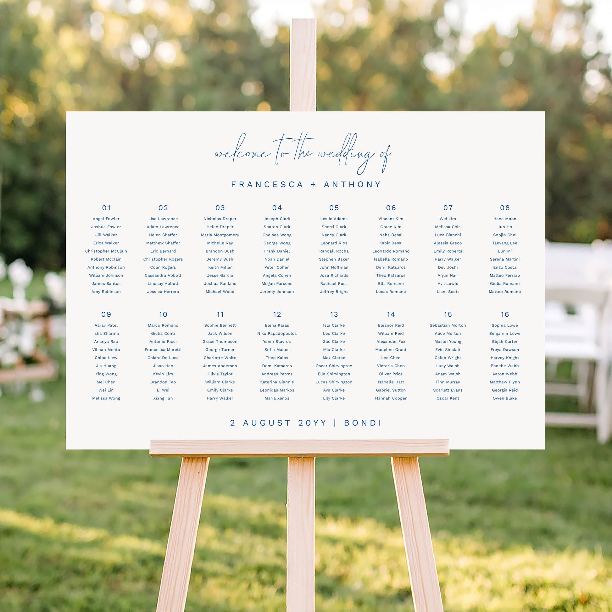 Modern 16-table landscape wedding seating plan on an easel in an outdoor wedding setting.