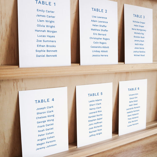 Set of six printable seating chart cards with names on a wooden display shelf.