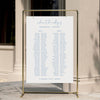 Minimal wedding seating chart template displayed on a gold stand against a neutral wall.