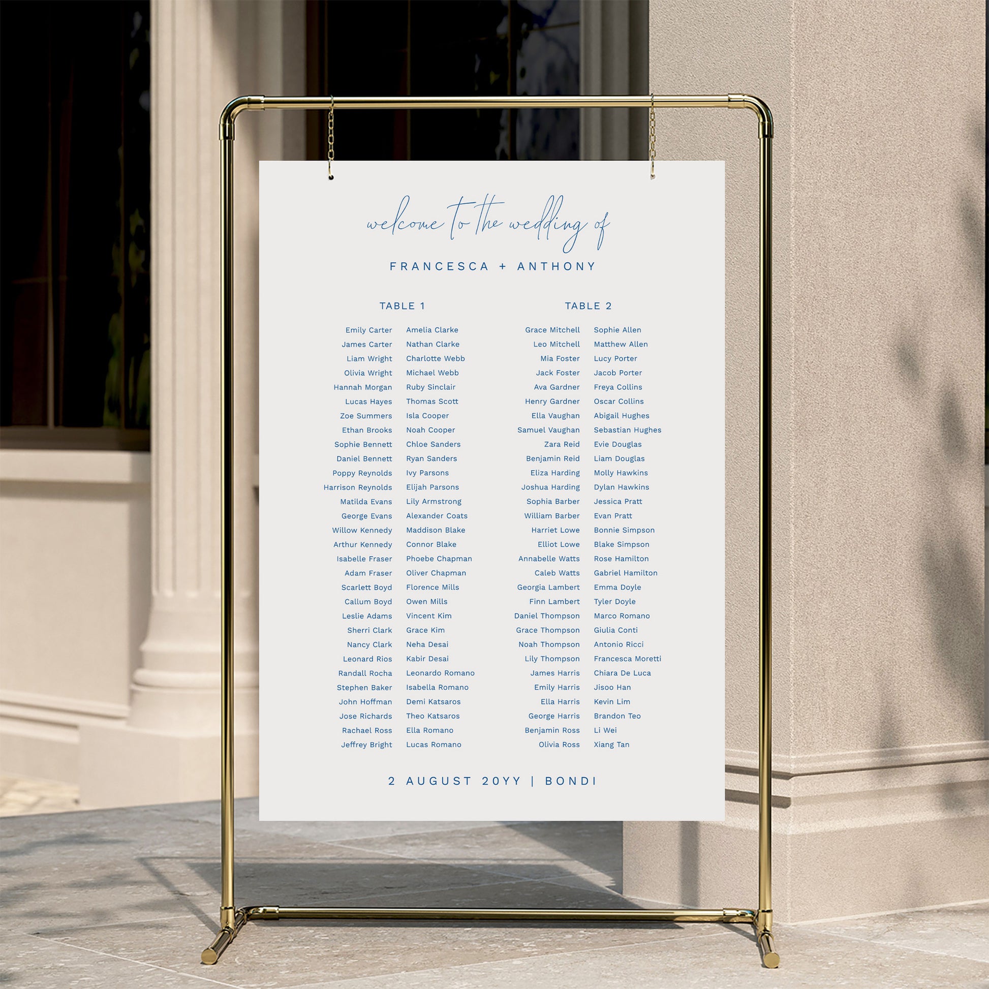 Minimal wedding seating chart template displayed on a gold stand against a neutral wall.