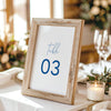 Printable table number card displayed on a wooden stand on a linen table cloth.