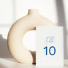 Beige ceramic circle vase with a white card displaying a table number on a light background.