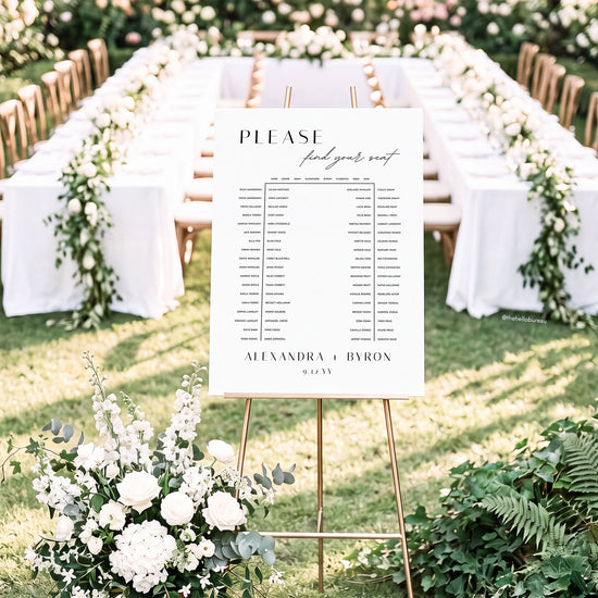 Printable horseshoe wedding seating chart on an easel in front of a u-shaped table setting with white florals