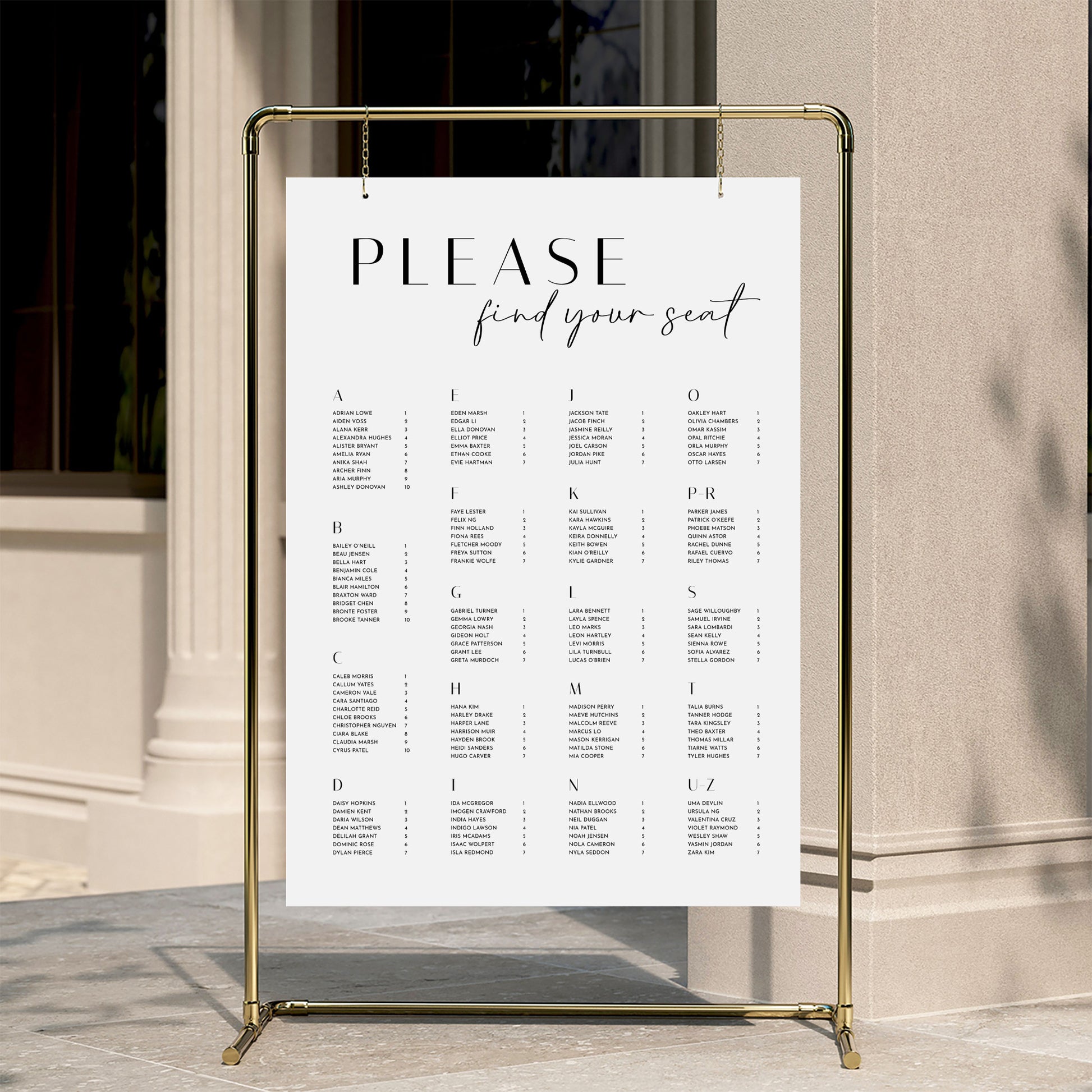 Alphabetical wedding seating chart template displayed on a gold stand against a neutral wall.