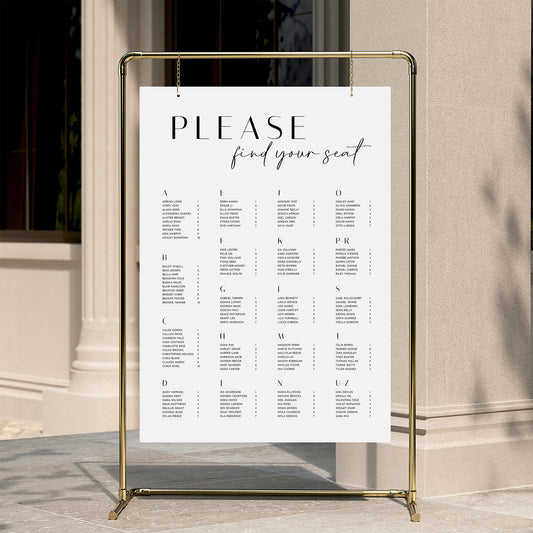 Alphabetical wedding seating chart template displayed on a gold stand against a neutral wall.