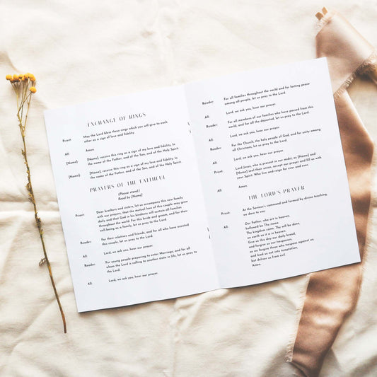 Open A5 wedding Mass ceremony booklet displaying interior ceremony text on a neutral fabric background.