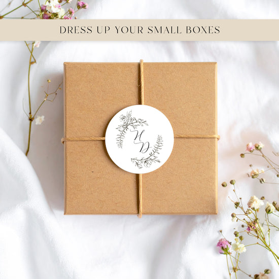Kraft paper box with a round monogram sticker on a white background with floral elements.