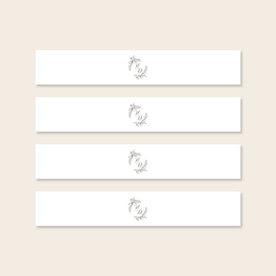 Four invitation belly bands with decorative monogram on a beige background.
