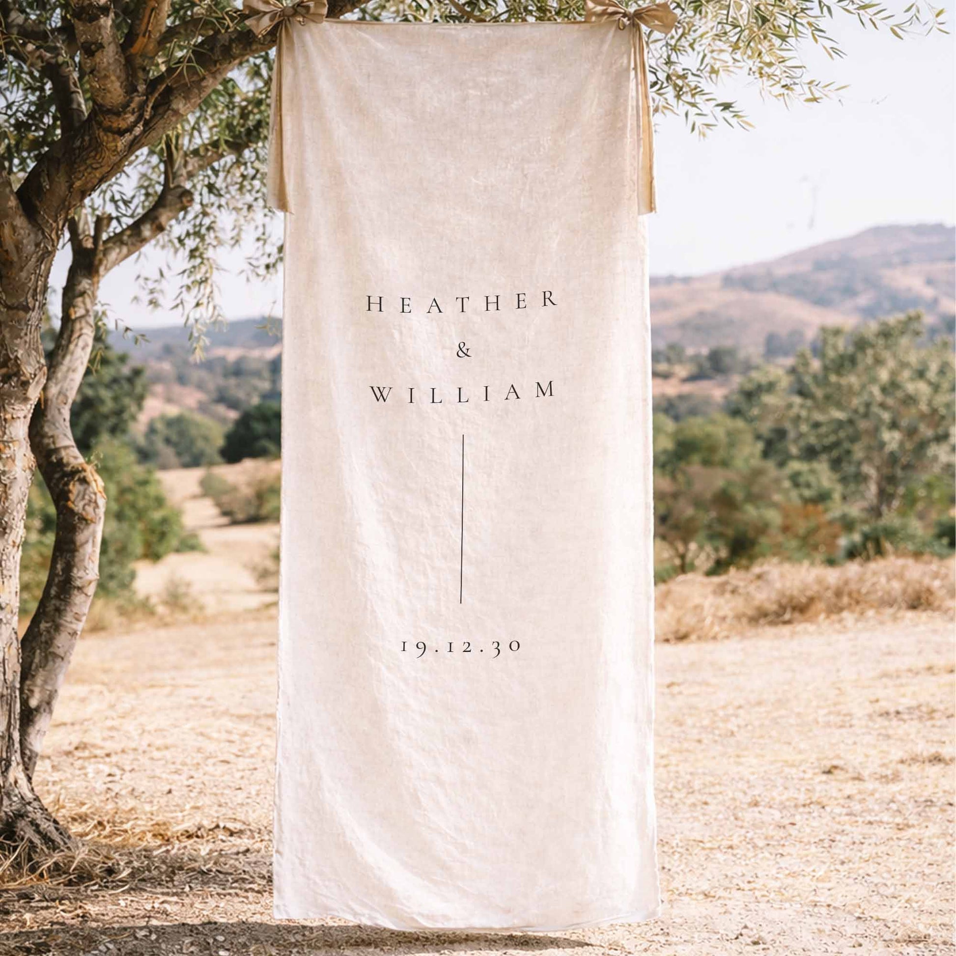 Linen welcome sign hanging from a tree in a scenic outdoor setting.