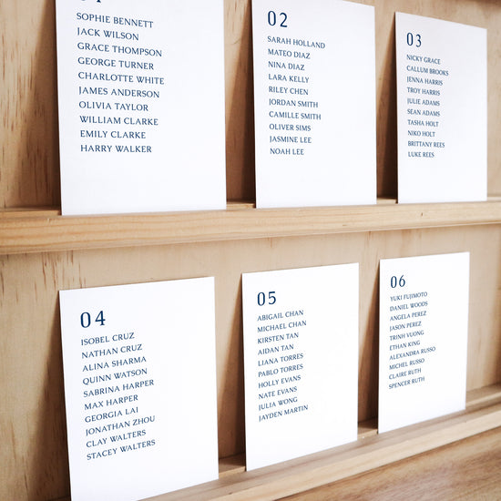 Set of six printable seating chart cards with names on a wooden display shelf.