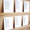Set of six printable seating chart cards with names on a wooden display shelf.