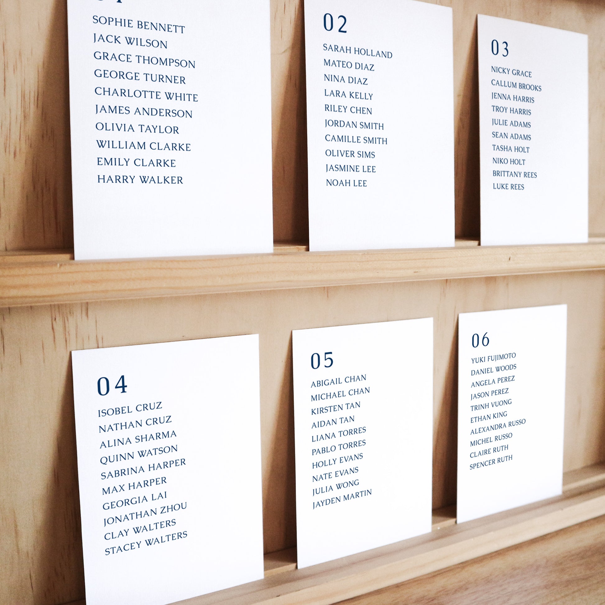 Set of six printable seating chart cards with names on a wooden display shelf.