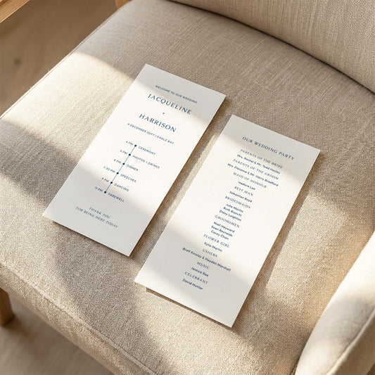 Two DL-sized wedding program cards laid flat on a cushioned chair with sunlight streaming across the linen fabric.