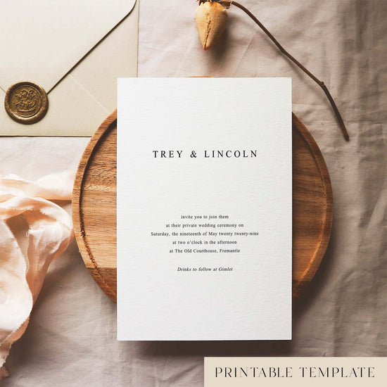 Wedding invitation template design on a white card sitting on a wooden plate with decorative elements.
