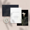 Wedding invitation card with black envelope and calla lily artwork on a beige background.