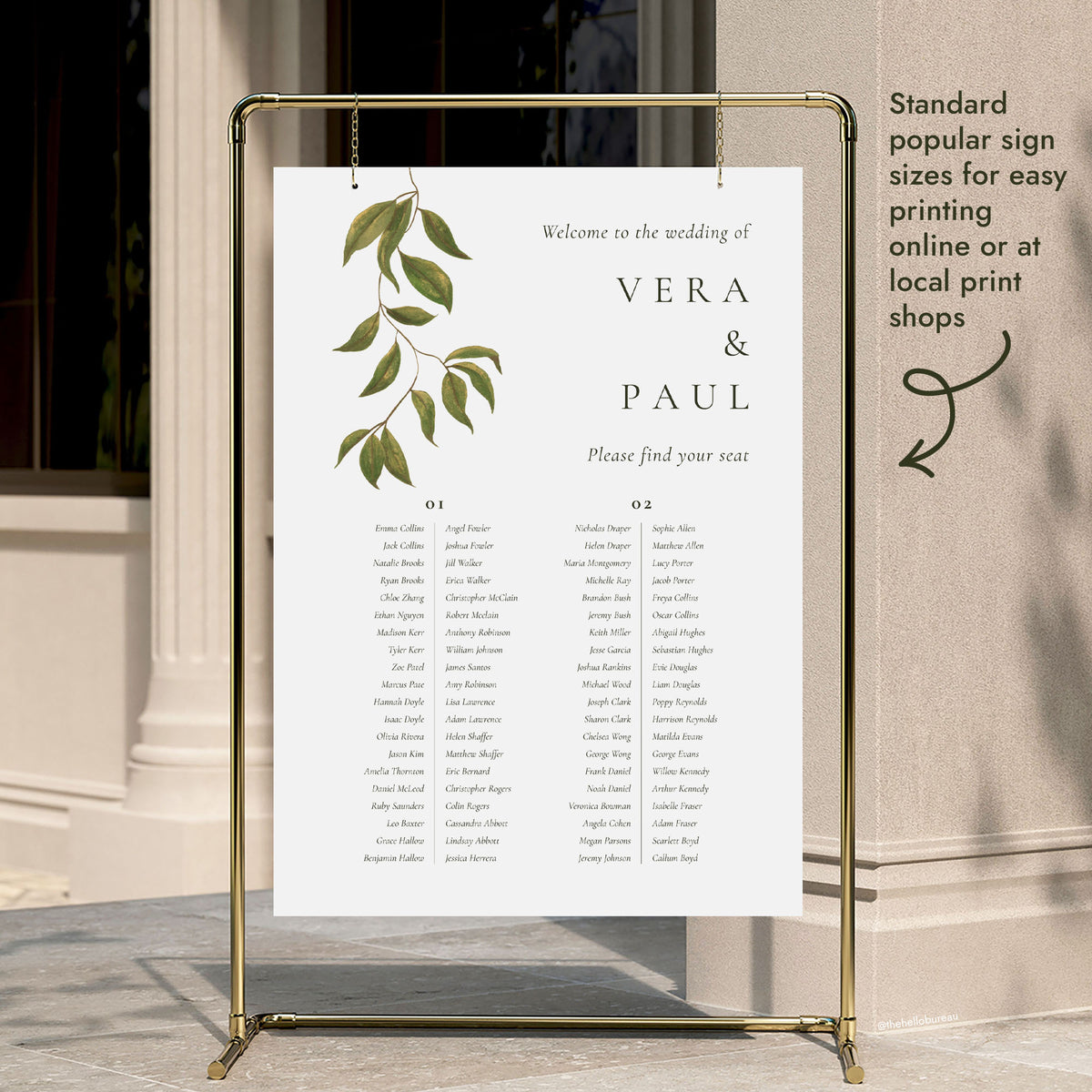 A 2-long-table wedding seating chart template hung on a gold display stand outside a modern city building entrance