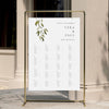 Alphabetical wedding seating chart template displayed on a gold stand against a neutral wall.
