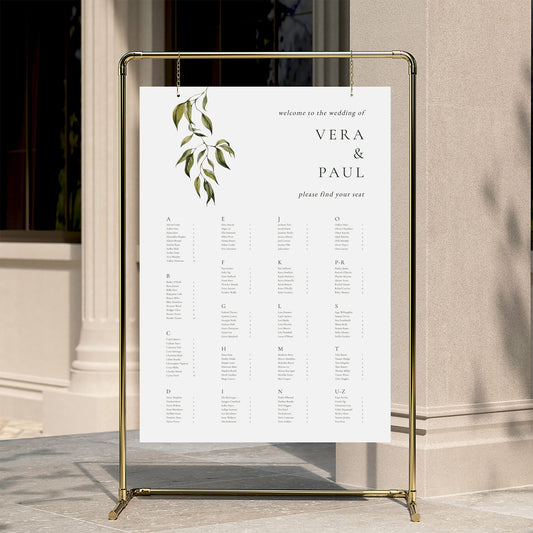 Alphabetical wedding seating chart template displayed on a gold stand against a neutral wall.