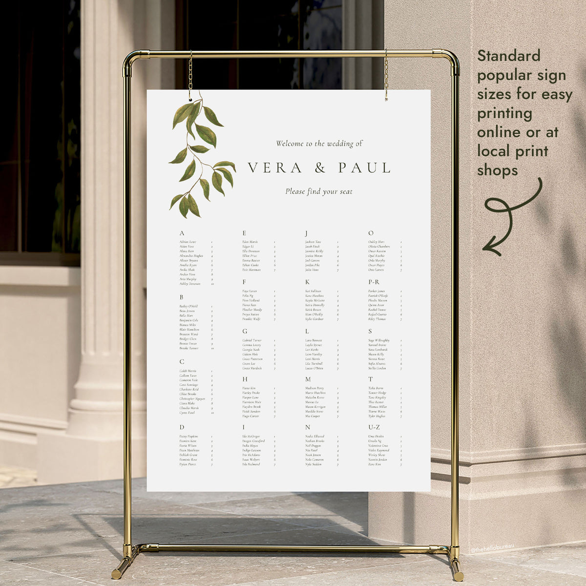An A to Z wedding seating chart template hung on a gold display stand outside a modern city building entrance
