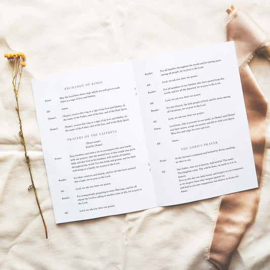 Open A5 wedding Mass ceremony booklet displaying interior ceremony text on a neutral fabric background.
