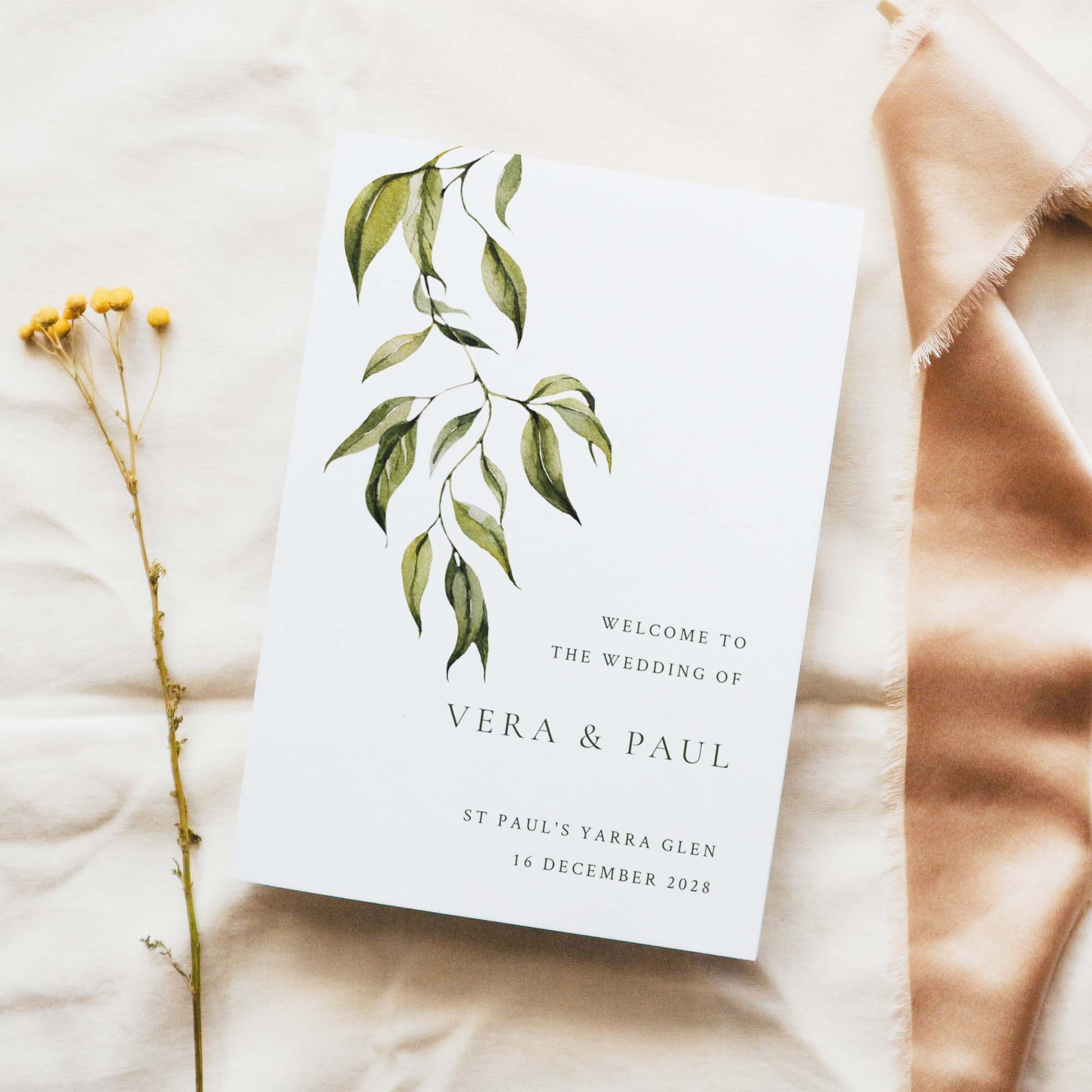 A5 wedding Mass ceremony booklet cover, photographed on light fabric with minimal floral styling.