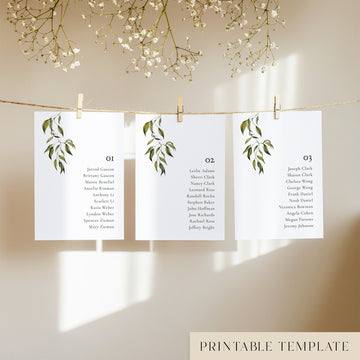 Three white seating chart cards with printed names and leaf design, clipped to a string with pegs, against a neutral background.